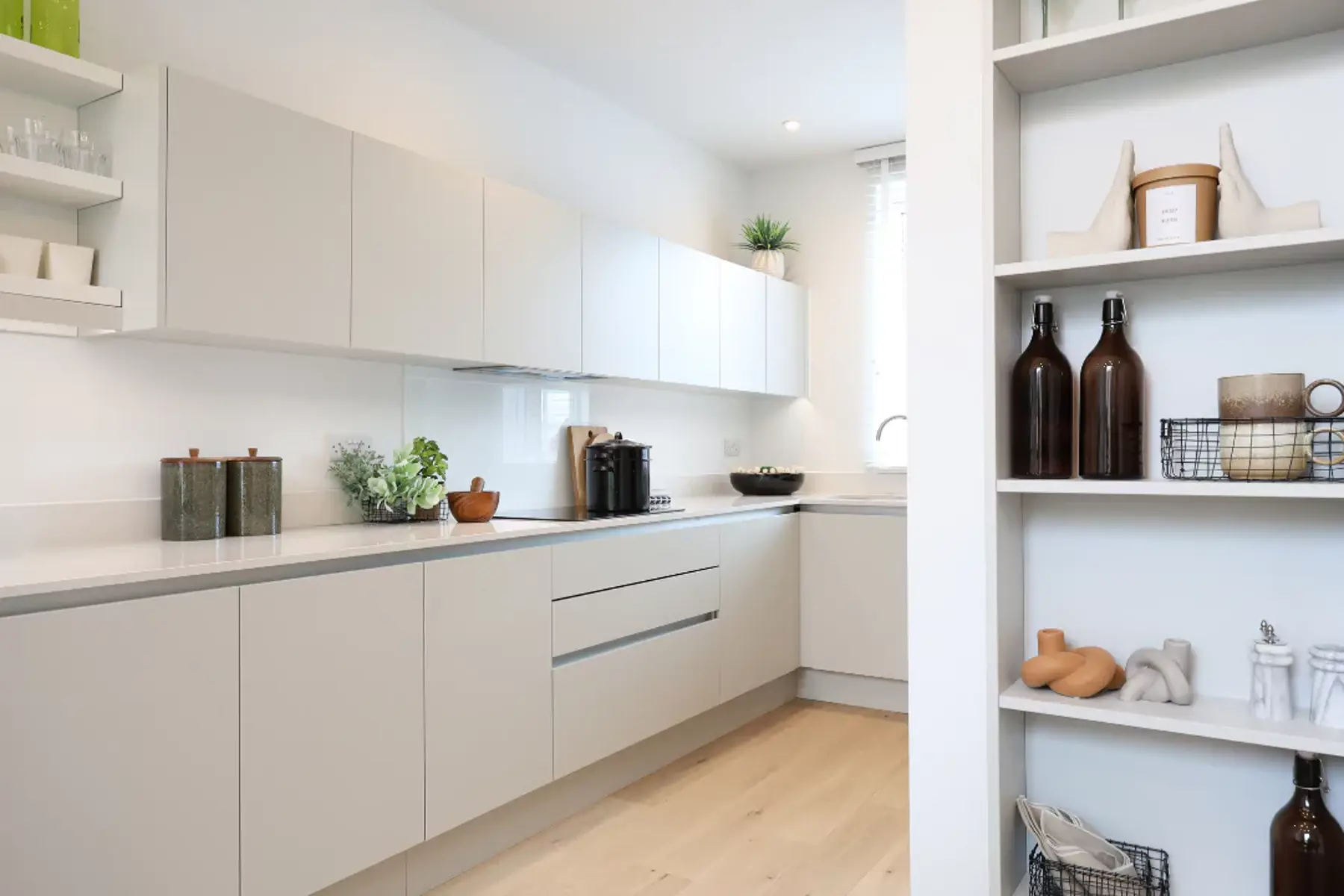 A long shot of a stylish kitchen with white work tops and ample storage.