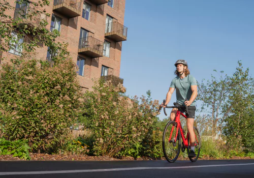 Young male cycling along a landscaped cycle path at Brabazon in Bristol on a red road bike in shorts and a helmet.