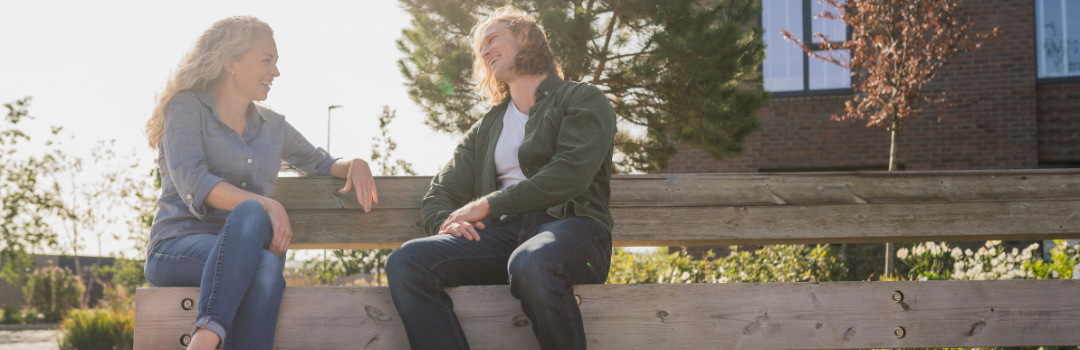 Man and woman conversing on a wooden park bench on a sunny day at Brabazon. 