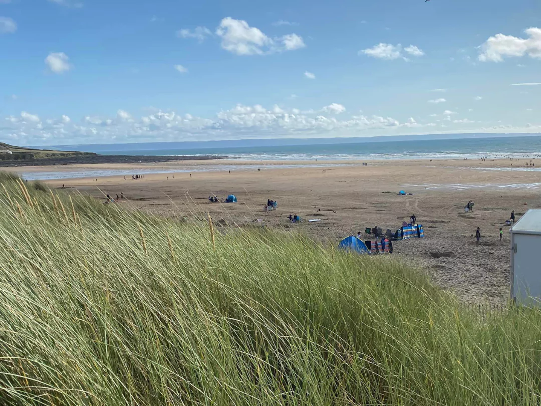 View of a flat beach with golden sand and beach tents, with sea and rocky headland in the distance