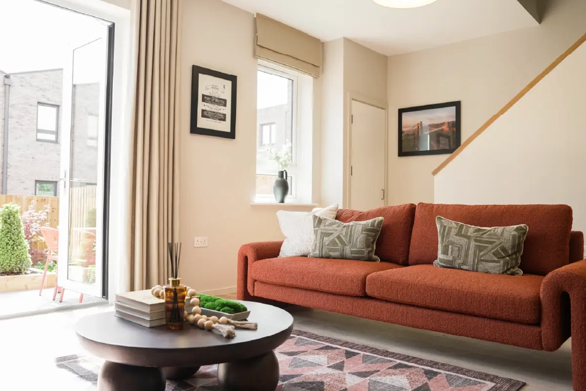 Modern living room featuring a rust-coloured sofa with patterned pillows, a round coffee table, and large windows opening to a garden.