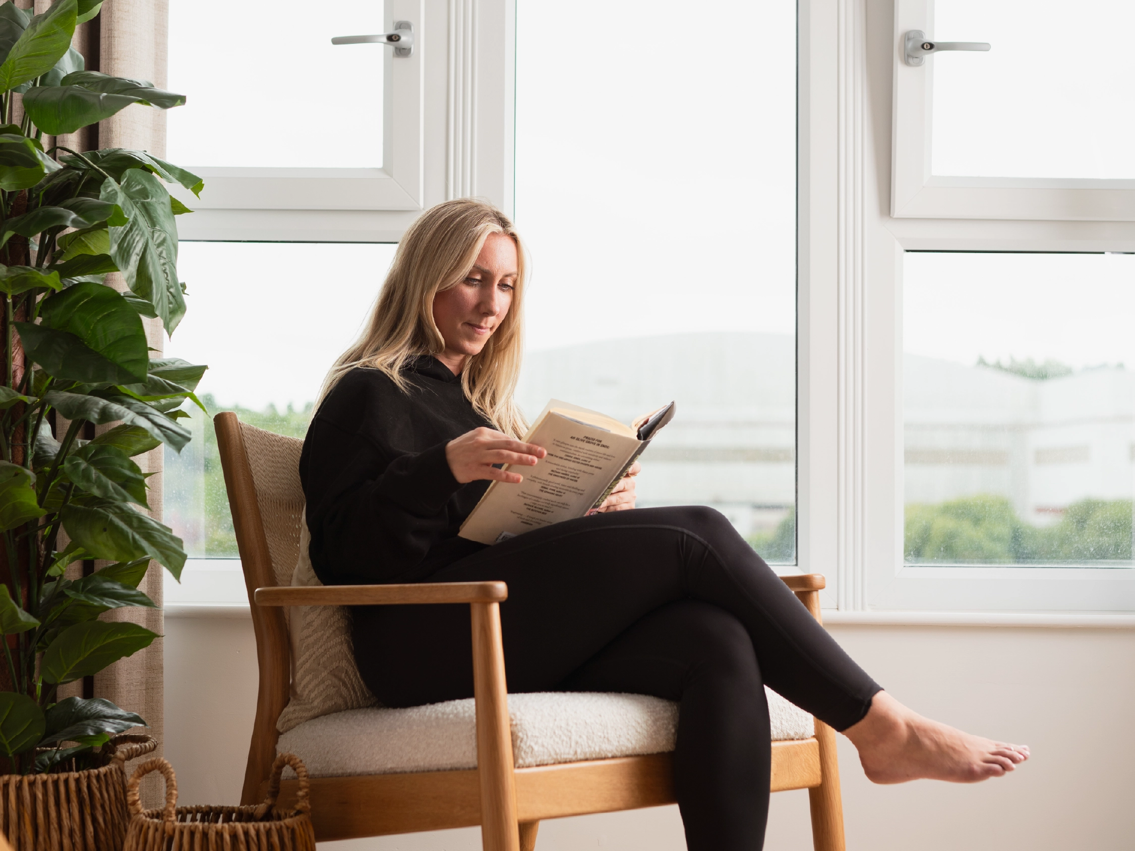 Woman sitting and reading her book next to double glazed window in home at Brabazon