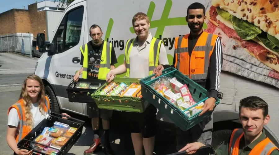 Group of young people in high-visibility vests and holding containers of food in front of a delivery van.