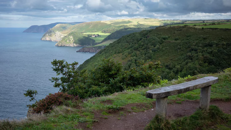 Empty wooden bench on the headland looking out to sea and the sunny coastline in the distance