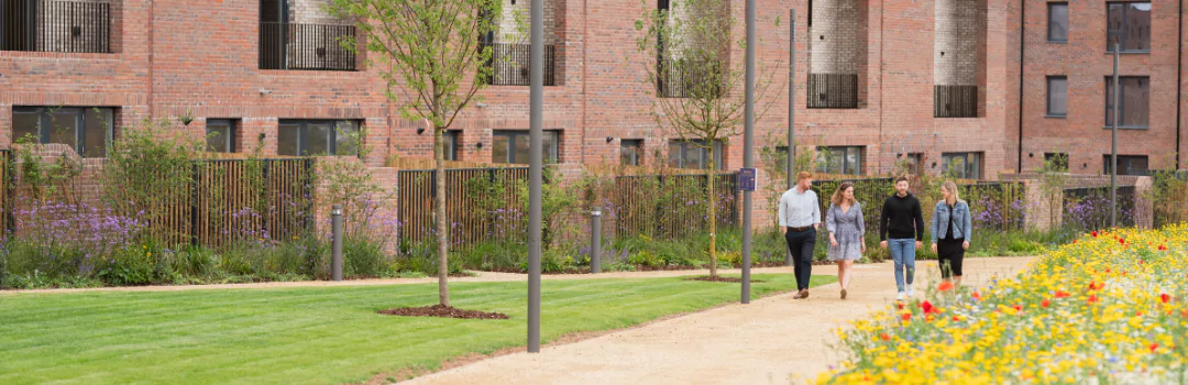 Four friends walking through a green park in a residential area, showcasing brick townhouses at The Heritage District at Brabazon. 