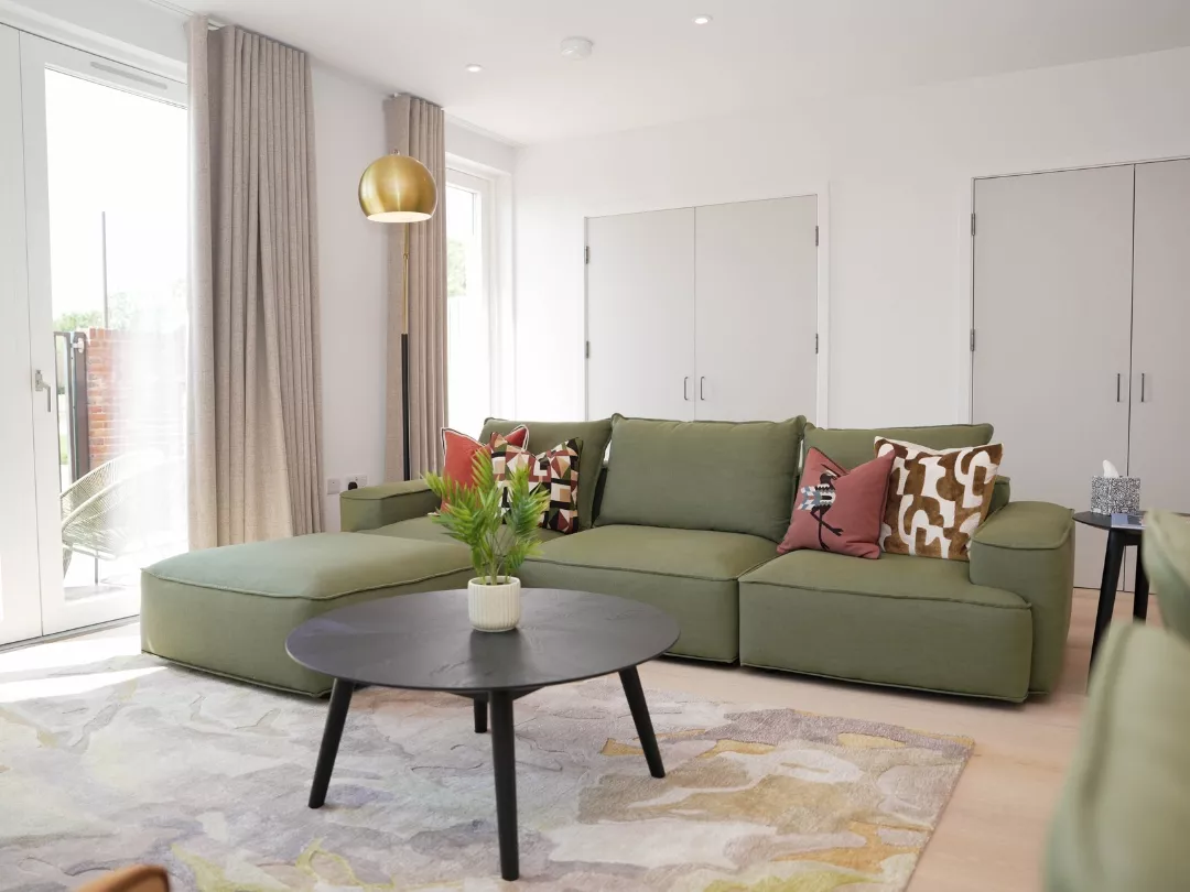 Modern living room inside light and bright home at  Brabazon,  showcasing a green sectional sofa adorned with patterned cushions, a round black coffee table, gold pendant lamp, and neutral furnishings.
