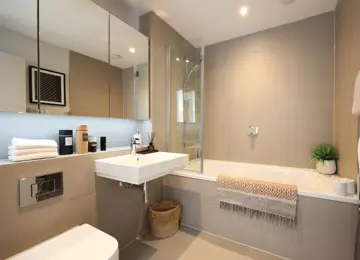 A wide angle of the family bathroom with added extras such as the large mirrored storage units and faux plants.