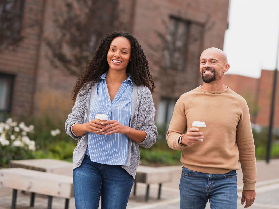 Young couple smiling and walking with takeaway coffee cups.