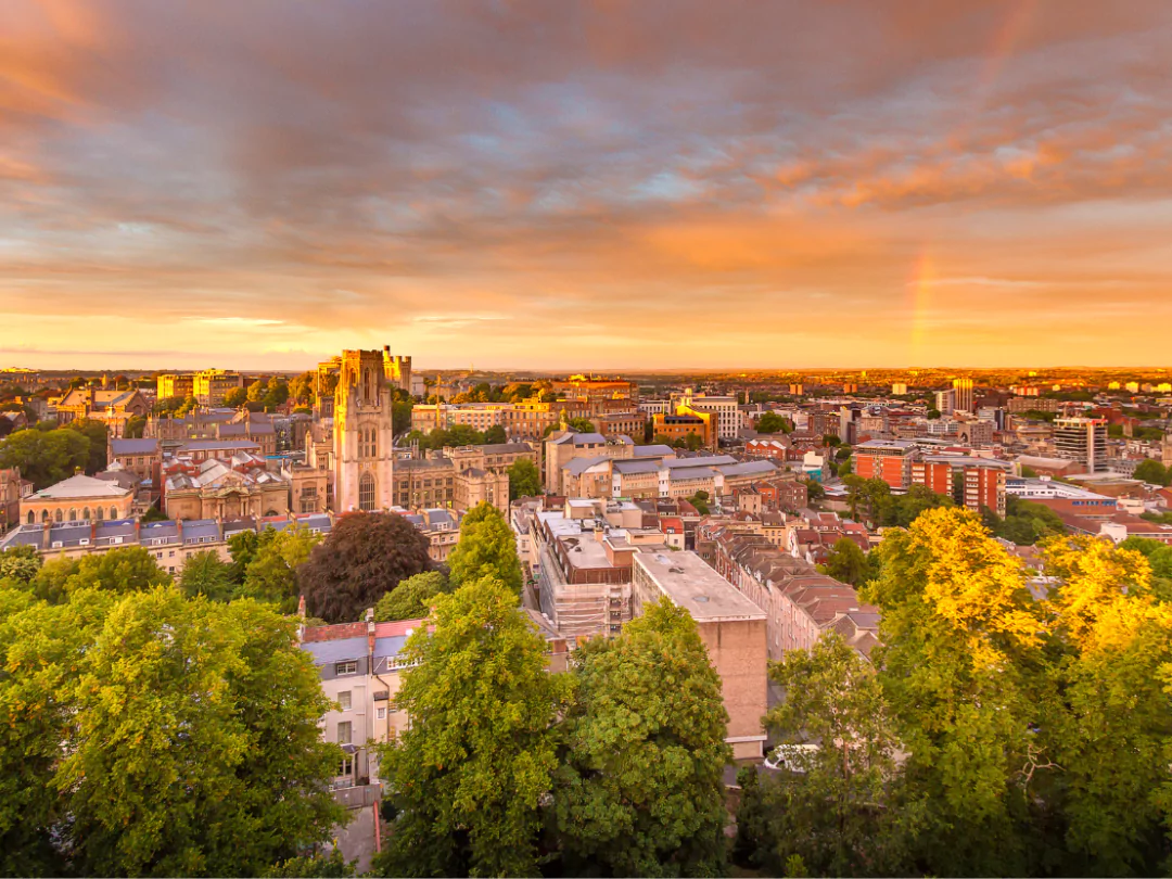 Rooftops and treetops of the city of Bristol bathed in orange sunlight in the late afternoon